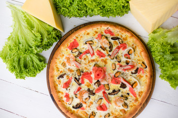 Delicious fresh Pizza with seefood (crabs and mussels) and cheese on the white wooden table surrounded by green salad and cheese