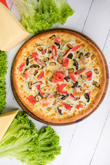 Delicious fresh Pizza with seefood (crabs and mussels) and cheese on the white wooden table surrounded by green salad and cheese
