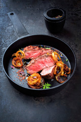 Modern Style classic dry aged sliced roast beef with fried onion rings served as closeup in a minimalistic design cast-iron skillet