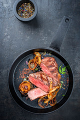Modern Style classic dry aged sliced roast beef with fried onion rings served as top view in a minimalistic design cast-iron skillet