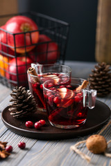 Mulled wine in glasses on a wooden background. Apples, cranberries, cinnamon, star anise, walnuts, cones