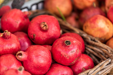 Closeup of fresh ripe, pink or red pomegranate round fruit, skin, whole in street farmer's market display bakset in Italy during summer, colorful vibrant