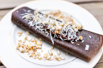 Macro closeup of chocolate crepe dessert wrap, rice crisps, coconut flakes, made in dehydrator with bananas on plate