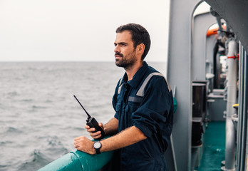 Marine Deck Officer or Chief mate on deck of vessel or ship . He holds VHF walkie-talkie radio in...
