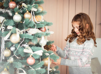 Little girl with curls decorates the Christmas tree. The child is happy to get ready for Christmas. Present. Winter.
