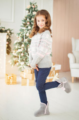 Merry Christmas and Happy New Year. Beautiful, little girl in New Year's environment. A child in a knitted sweater and knitted boots. Snow, a fairy tale, a miracle.