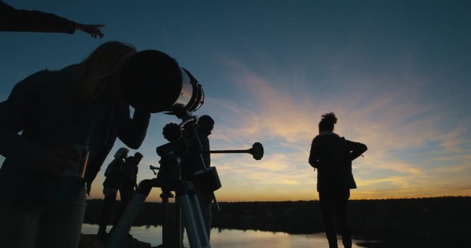 Low angle shot of friends stargazing together and using a professional telescope at night near a stream