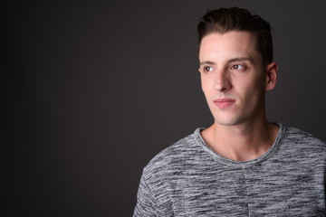 Face of young handsome man thinking against gray background