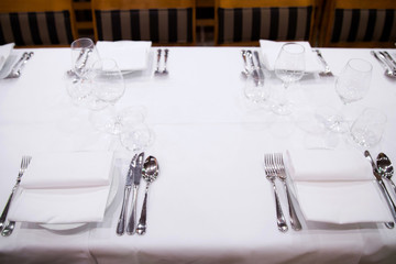 Beautifully decorated table with empty white plates, glasses and cutlery  on luxurious tablecloths