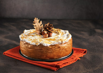 Homemade Pumpkin Cheesecake with Marshmallow Meringue Topping decorated with pinecones and autumn leaves over dark background. Autumn Decoration.