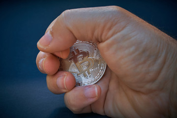 A hand grabs a bitcoin coin. The coin shines and reflects light. The background is dark and abstract. The BTC currency is the symbol of a decentralized cryptocurrency.