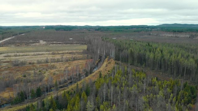 Aerial, drone shot, towards a river, surrounded by leafless, autumn forest and fields, on a cold, cloudy, fall day, in Juuka, North Karelia, Finland