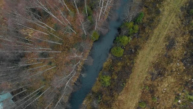 Aerial, rising screwdriver, drone shot, above a river, surrounded by leafless, autumn forest, on a cold, cloudy, fall day, in Juuka, North Karelia, Finland