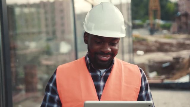 Smiling Afro-American construction manager using tablet then looking straight to camera and brightly smiling. Happiness, professional, browsing the internet. Technologies. Male portrait