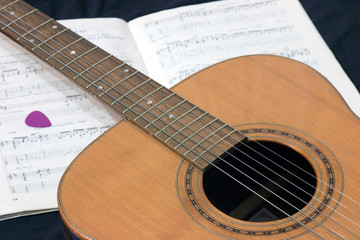 Fototapeta na wymiar acoustic guitar on the background of a music book with notes and pick