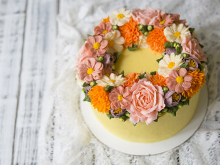 Yellow cream cake decorated with buttercream flowers - peonies, roses, chrysanthemums, scabiosa, carnations - on white wooden background. Close up, copy space