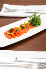 A dish of sockeye salmon crudo on a white plate with fresh herbs.