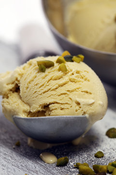 Pistachio ice cream scoop with chopped nuts and white chocolate on a rustic background.