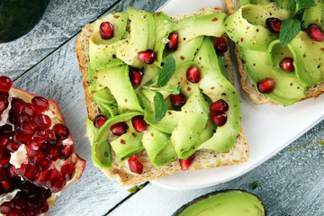 sliced avocado and ripe pomegranates on toast bread with spices and avocado.