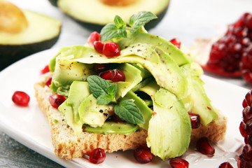 sliced avocado and ripe pomegranates on toast bread with spices and avocado.