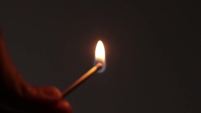 Person striking a match in darkness. The match is lit and the flame lights up the frame. Hands only shot.