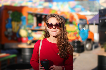  young woman at a street food festival with a glass of coffee. long-haired girl in a red dress.