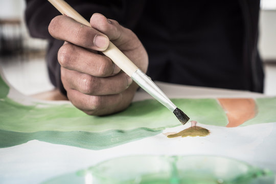 Hands asian student artist painting watercolor abstract of landscape with brush drawing on paper for creation art subject classroom at secondary education in Thailand. Creative skill, Hobbies concept