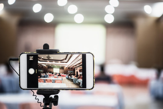 Blurred of live smartphone Video camera or camcorder operator working for record couple speaker or Presenterson stage in conference and convention hall blur light bokeh background