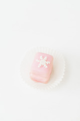 Light pink petit fours, small cake square, covered with sugar icing and decorated with white fondant snowflake