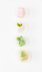 White, light pink, yellow and green petit fours, small cake squares decorated with fondant, chocolate, sugar icing and marzipan Christmas ornaments