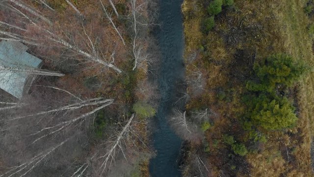 Aerial, drone shot, close to the trees, above a river, surrounded by leafless, autumn forest, on a cold, cloudy, fall day, in Juuka, Pohjois-Karjala, Finland