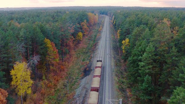 Aerial view of a freight train carrying coal and rubble through the autumn forest