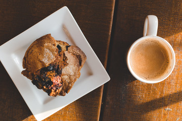 Above view of a blueberry muffin and a cup of coffee latte on a wood table with rays sunlight.