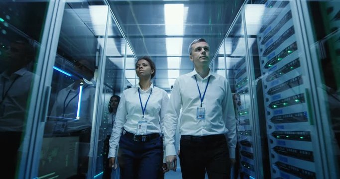 Wide shot of workers in a data center walking between rows of server racks on their way to a meeting