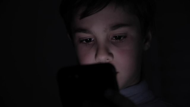 Closeup of Young Happy Boy Face looking at Smartphone at Night at Home