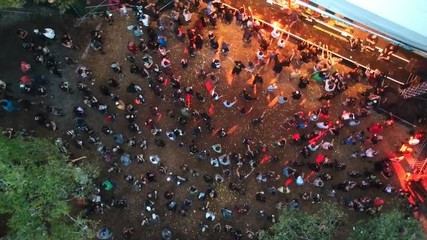 Aerial drone shot of a crowd watching an outdoor concert event at a festival with flashing lights in a forest.