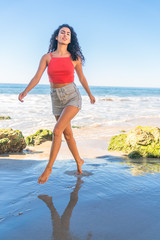 Portrait of latino woman with curly hair, red top and denim shorts running at beach