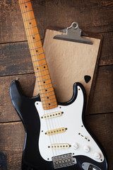 Fototapeta premium Vintage black double cutaway guitar on old wood surface and old clipboard, good for play lists, and production notes. one piece maple neck.