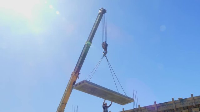 A man directs a concrete slab raised by a truck crane