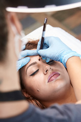 microblading, woman drawing with pencil eyebrow shape. elevated view.
