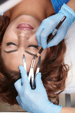 microblading, woman drawing with pencil eyebrow shape, checking it with caliper. elevated view.