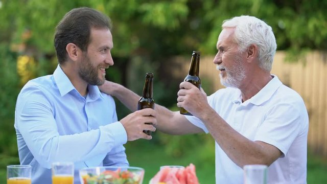 Senior and middle-aged men clinking beer bottles and talking, brewing traditions