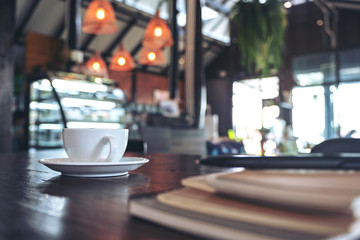 Closeup image of a white cups of hot coffee and notebooks on vintage wooden table in cafe