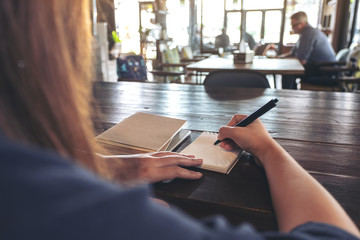 Closeup image of a woman writing on blank notebook on table in cafe