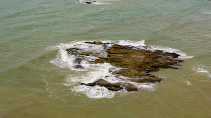 Aerial drone view of waves breaking against rocky next to a lighthouse