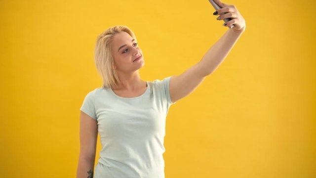 Happy blond model size plus make selfie on her phone at yellow background slow motion