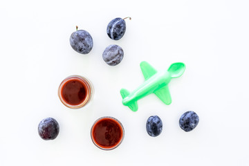 Fruit puree for small babies. Puree with prunes in bowl near punes, spoon, toy on white background top view copy space