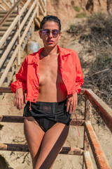 Portrait of latino woman with curly hair, orange jacket and yellow glasses at beach