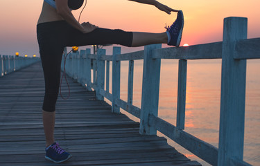 slim fit woman pre exercise before running jogging on the wooden pier at light of sunset, healthy woman work out daily exercise
