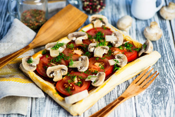 puff pastry pie with tomatoes and mushrooms on a wooden board